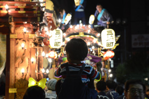 電飾の灯った山車と子どもの背中